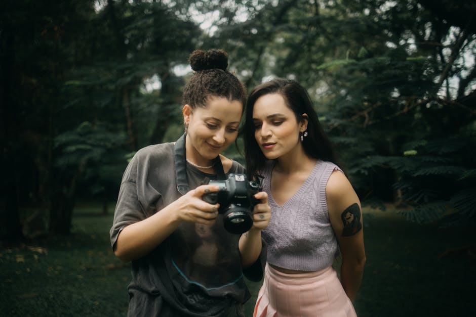 Two women in a park reviewing photos on a digital camera, enjoying outdoor photography.